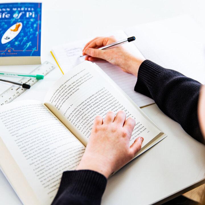 Hands resting on an open paperback beside a notebook, with a copy of Life of Pi on the table